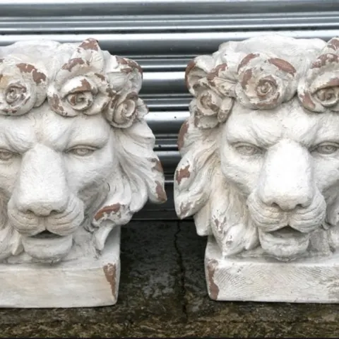 A pair of distressed painted urns in the form of lion heads
